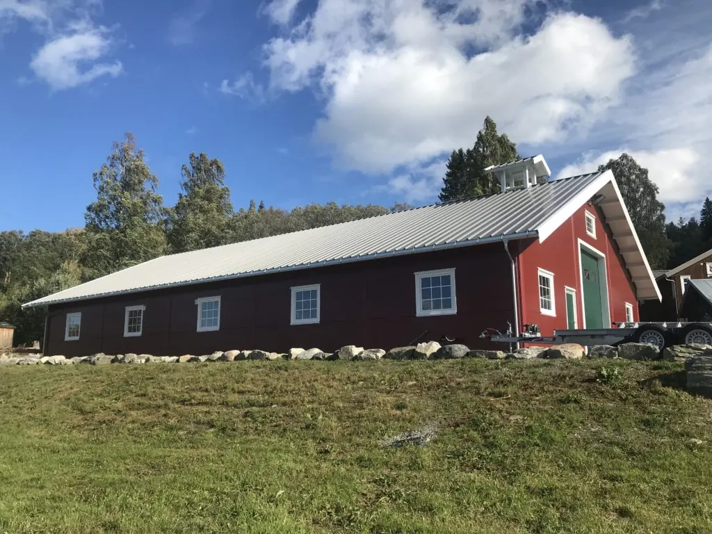Rødt lagerbygg med hvite vinduer og grønn port på Amundrud